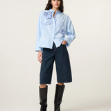 Vue en pied de la blouse ample bleu clair FABIENNE CHAPOT portée avec un bermuda en jean et des bottes hautes