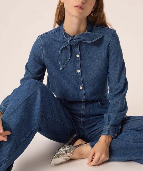 Modèle assise portant la blouse en denim fluide Lenora DES PETITS HAUTS avec col bandana à nouer avec un jean et des chaussures metallisées