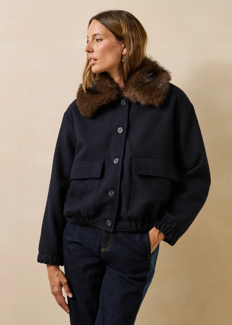 Mannequin portant le blouson bomber marine Galane LA FÉE MARABOUTÉE avec son col fausse fourrure marron et un jean brut