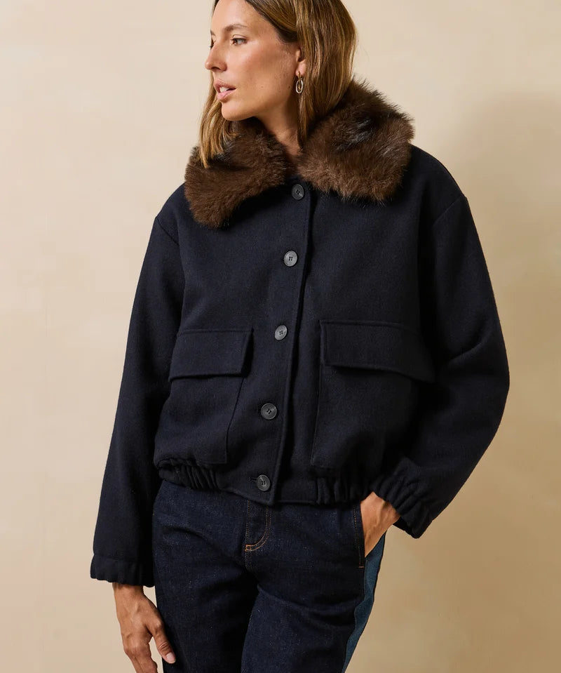 Mannequin portant le blouson bomber marine Galane LA FÉE MARABOUTÉE avec son col fausse fourrure marron et un jean brut