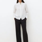 Silhouette complète avec la chemise blanche CAROLL Cira portée avec un pantalon de tailleur noir