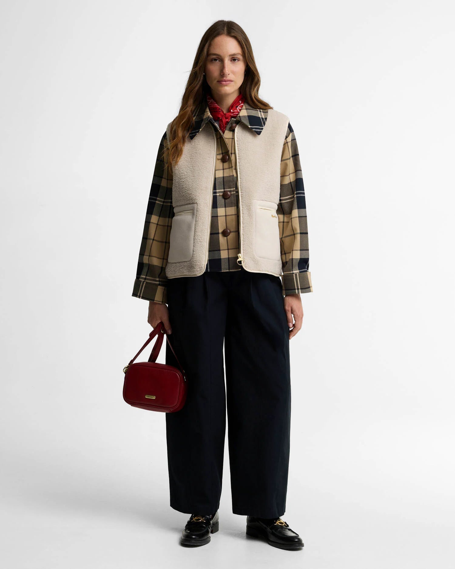 Look complet avec le gilet moumoute Bainford BARBOUR beige, surchemise à carreaux, pantalon large noir et sac rouge