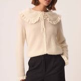 Modèle portant le gilet crème Carlie DES PETITS HAUTS à col Claudine volanté avec un pantalon sombre