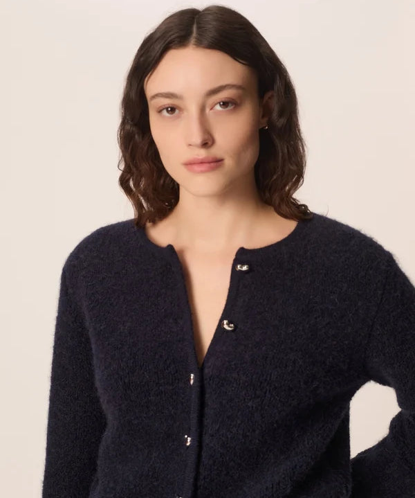 Modèle accroupi mettant en valeur la maille bouclée et les manches du gilet marine Cumin DES PETITS HAUTS