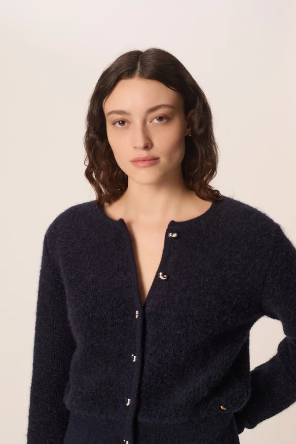 Modèle accroupi mettant en valeur la maille bouclée et les manches du gilet marine Cumin DES PETITS HAUTS