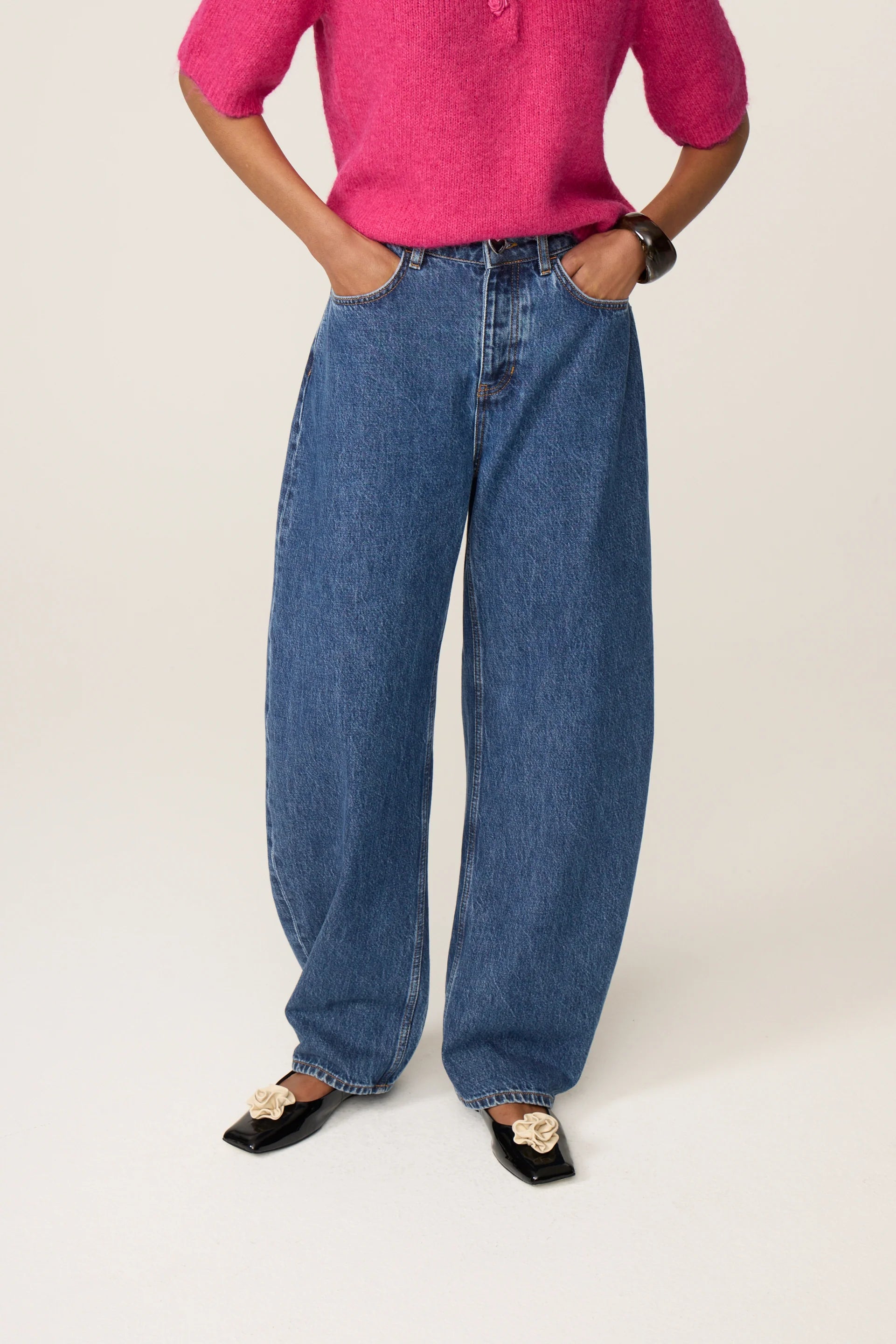 Visuel porté des jambes et des pieds du jean délavé bleu moyen FABIENNE CHAPOT Betty Barrel avec un pull rose