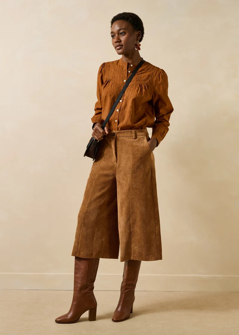 Silhouette complète portée avec le bermuda large cognac Galiope LA FÉE MARABOUTÉE, chemisier fluide et bottes à talons