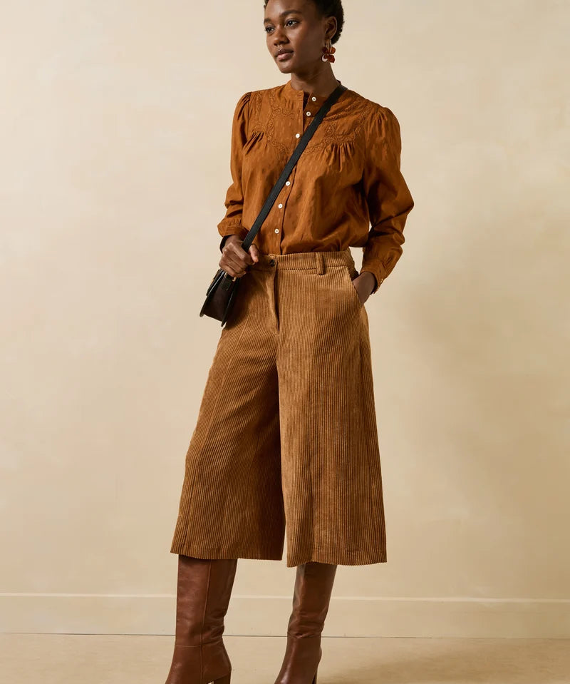 Silhouette complète portée avec le bermuda large cognac Galiope LA FÉE MARABOUTÉE, chemisier fluide et bottes à talons