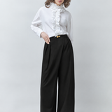 Silhouette complète du pantalon large noir SUNCOO FEMME Jupiter porté par un mannequin avec une chemise blanche à volants