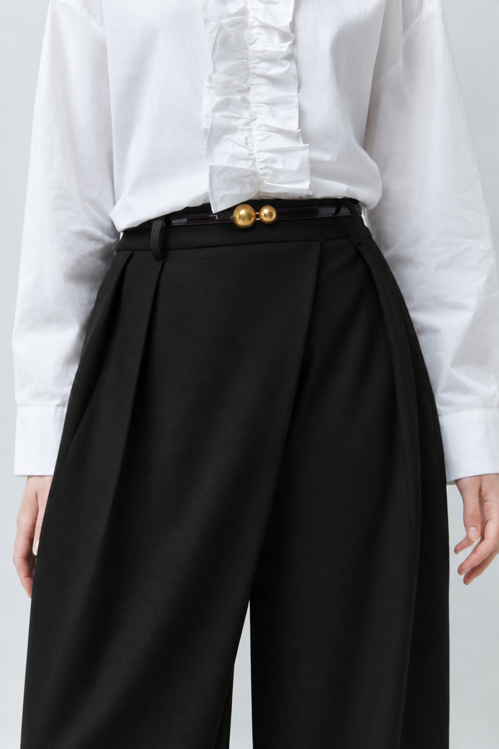Zoom sur la taille haute et le drapé croisé du pantalon noir SUNCOO FEMME Jupiter porté avec une ceinture fine dorée