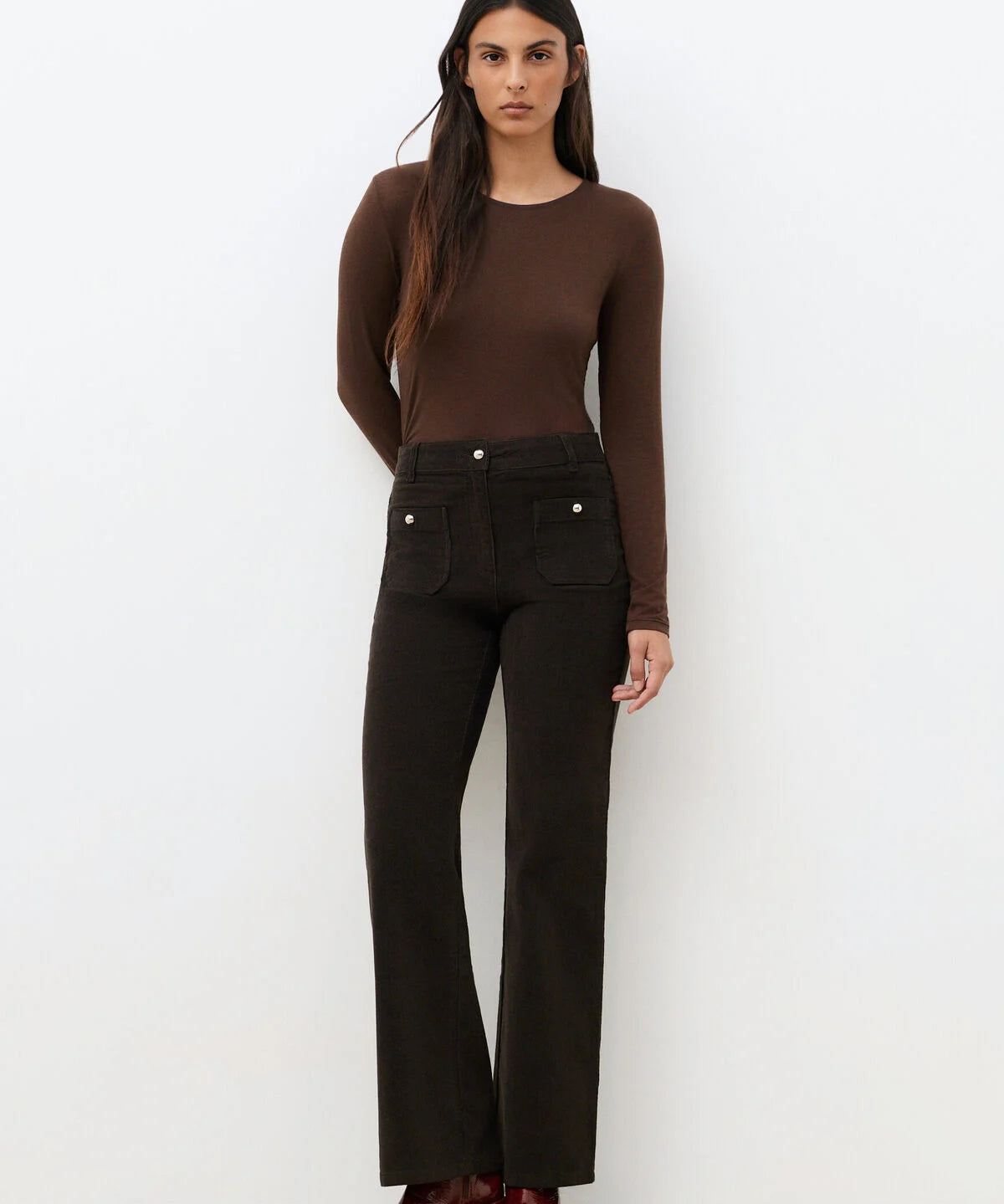 Pantalon bootcut en velours côtelé marron foncé CAROLL Pelley avec poches plaquées boutonnées porté avec un top marron et des bottines
