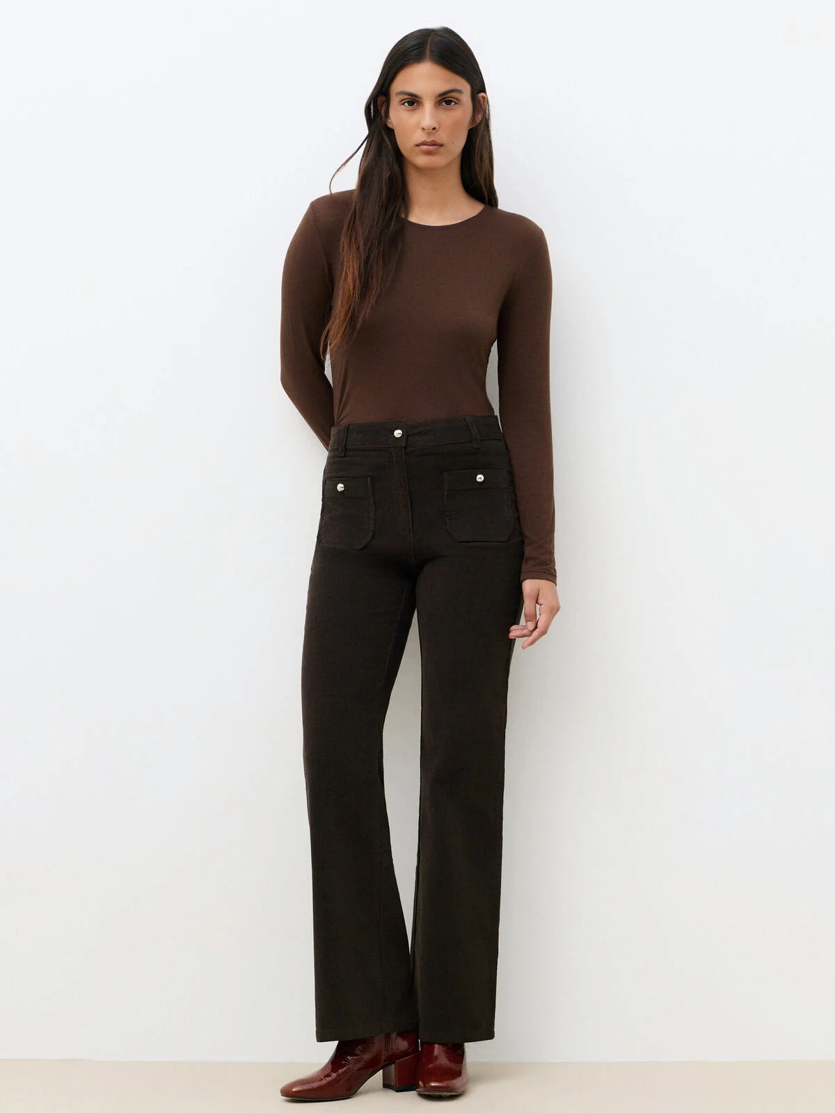 Pantalon bootcut en velours côtelé marron foncé CAROLL Pelley avec poches plaquées boutonnées porté avec un top marron et des bottines
