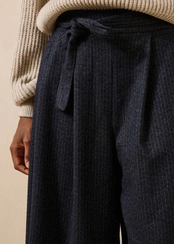 Zoom sur le tissu à fines rayures verticales mouchetées et le détail du nœud de la ceinture du pantalon Dactus