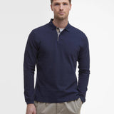 Portrait de face d'un homme portant le polo manches longues Essentiel bleu marine BARBOUR HOMME avec un pantalon beige