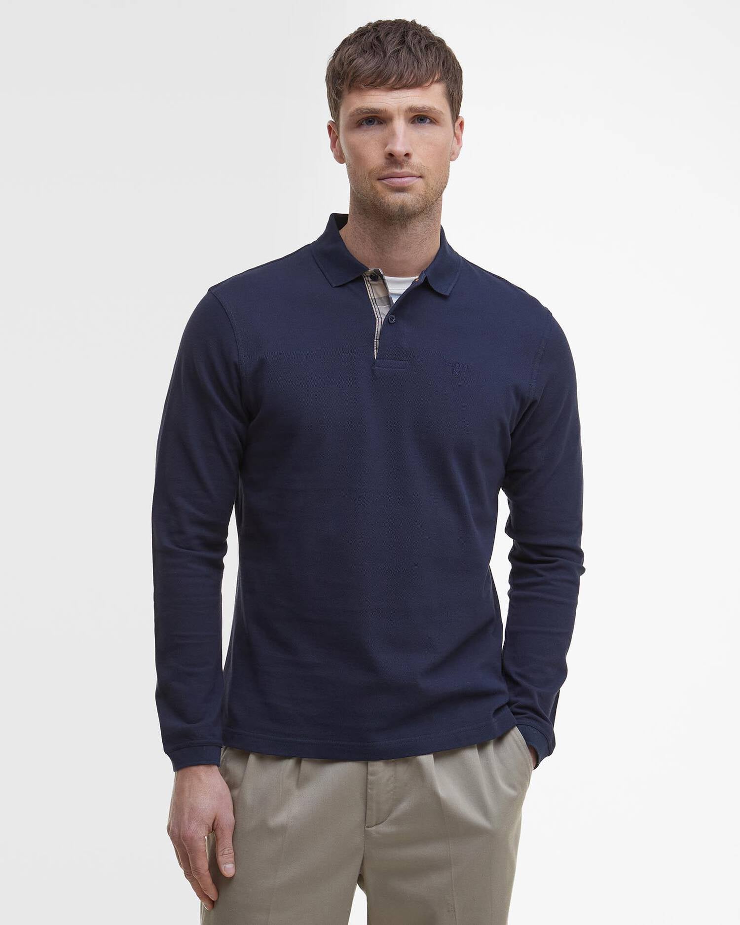 Portrait de face d'un homme portant le polo manches longues Essentiel bleu marine BARBOUR HOMME avec un pantalon beige