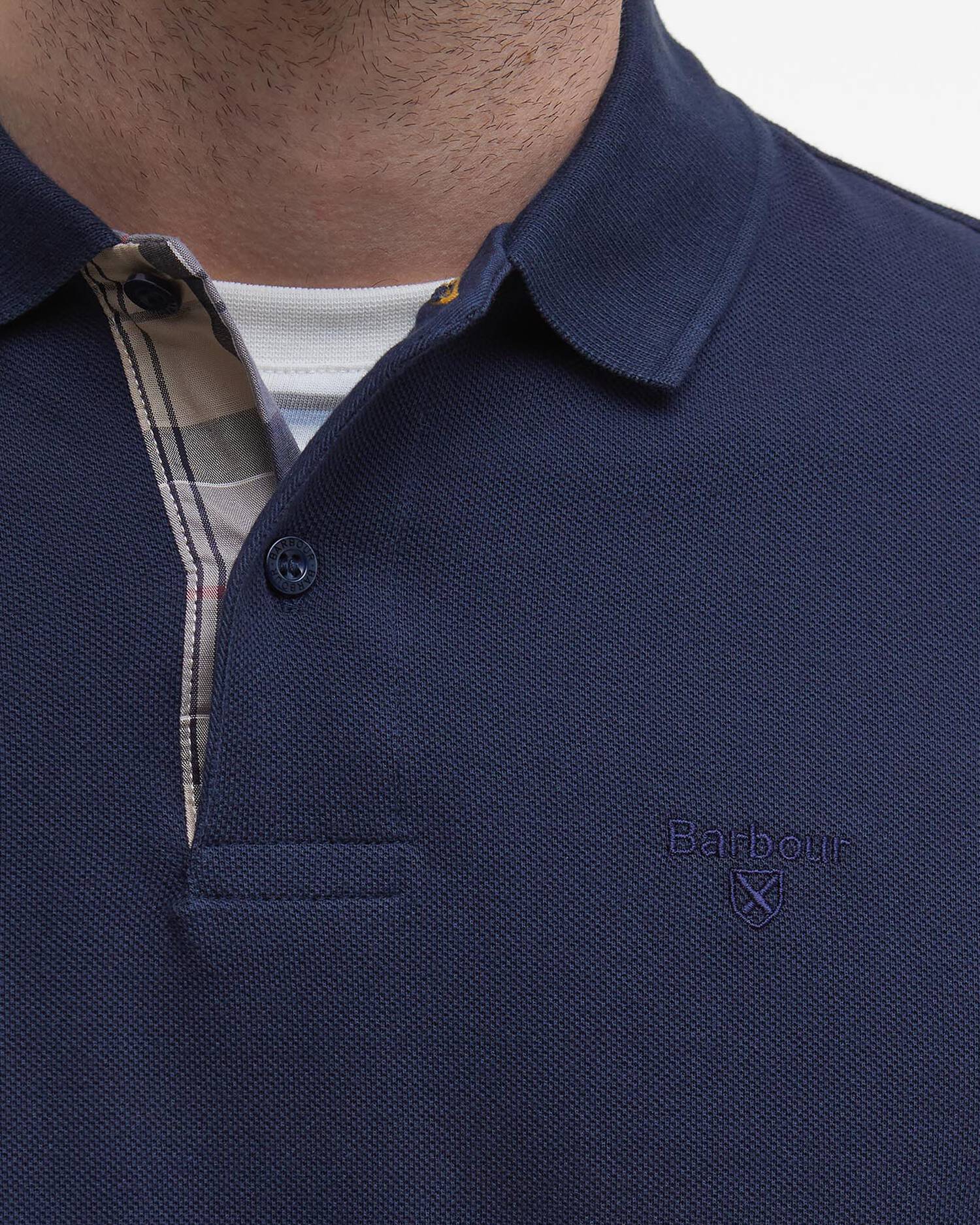 Zoom sur le col boutonné et la doublure tartan du polo bleu marine Barbour