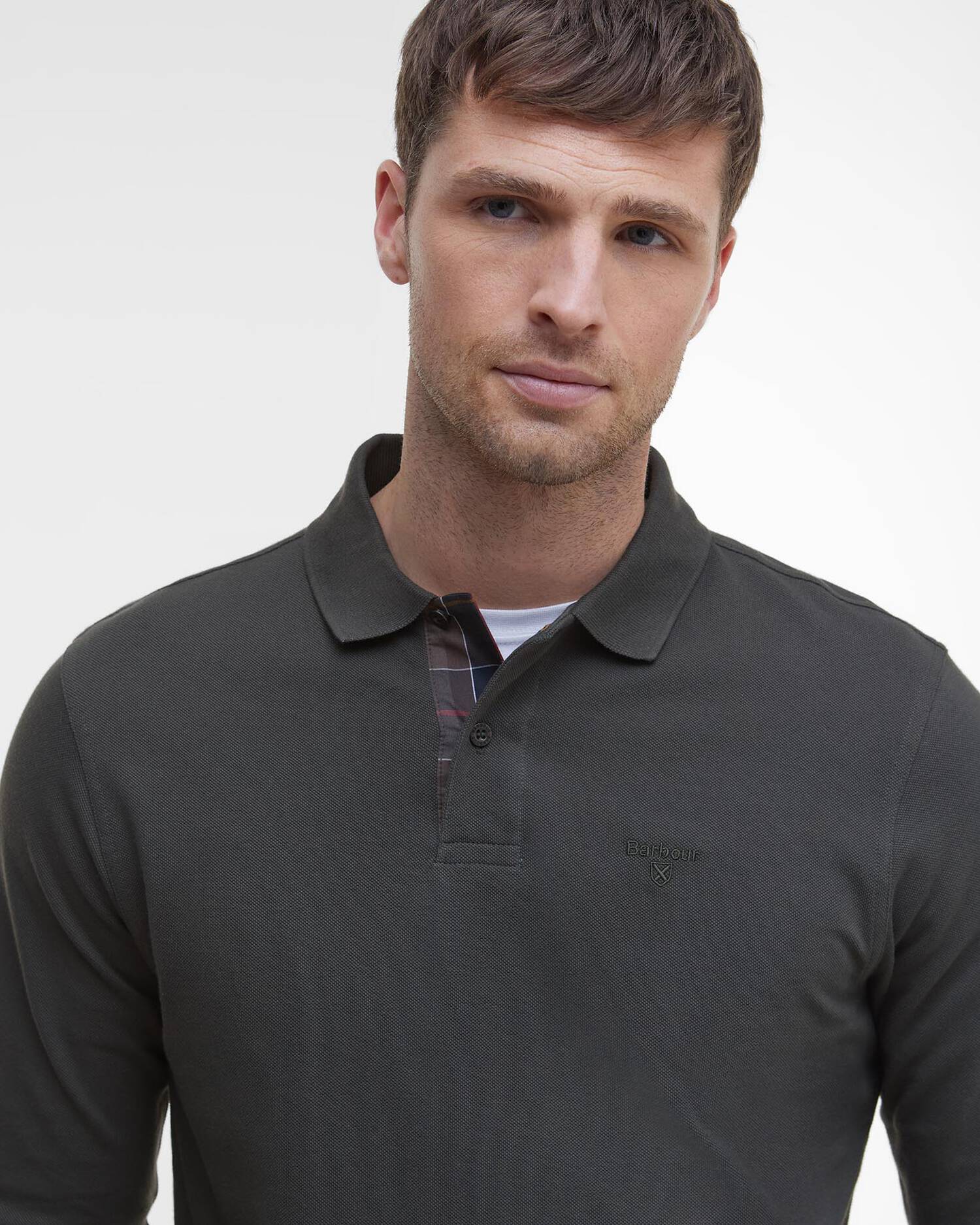 Gros plan sur le mannequin portant le polo vert forêt Barbour et laissant apparaître la doublure tartan