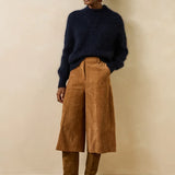 Silhouette d'un modèle portant le pull bleu encre Genesio LA FÉE MARABOUTÉE avec un pantalon large en velours et des bottes