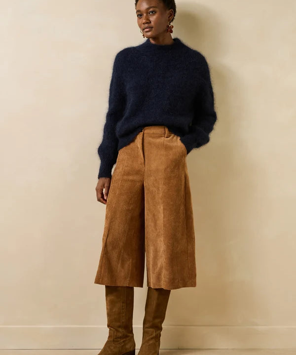 Silhouette d'un modèle portant le pull bleu encre Genesio LA FÉE MARABOUTÉE avec un pantalon large en velours et des bottes