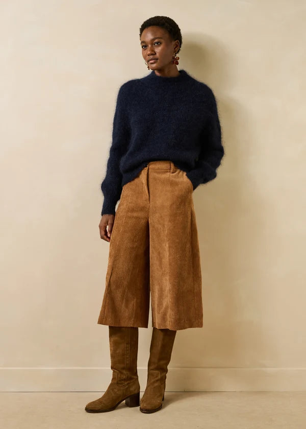 Silhouette d'un modèle portant le pull bleu encre Genesio LA FÉE MARABOUTÉE avec un pantalon large en velours et des bottes