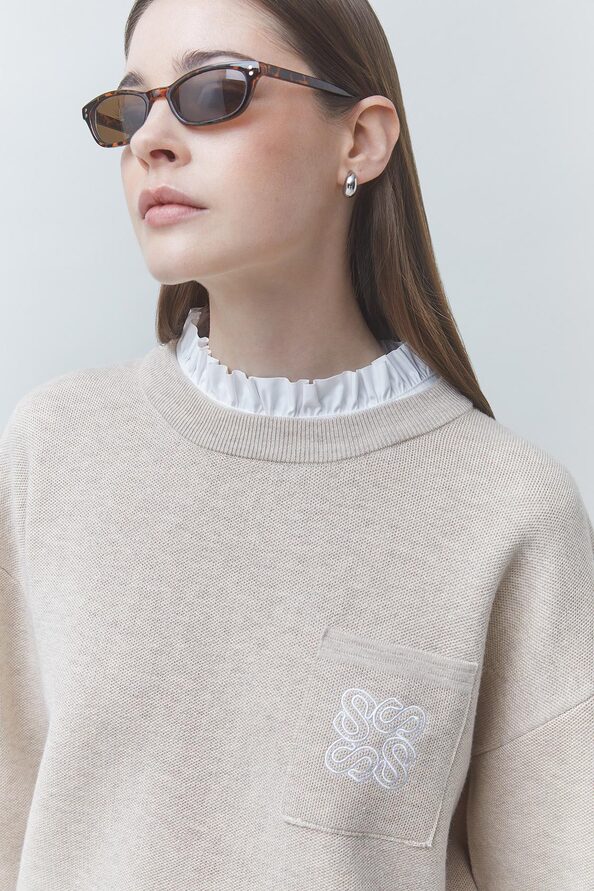 Gros plan sur la collerette plissée blanche et le logo brodé sur la poche du pull SUNCOO FEMME Pacoli