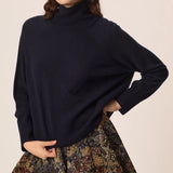 Modèle portant le pull col roulé marine Aramis DES PETITS HAUTS ajustant le bas du tricot avec une jupe fleurie