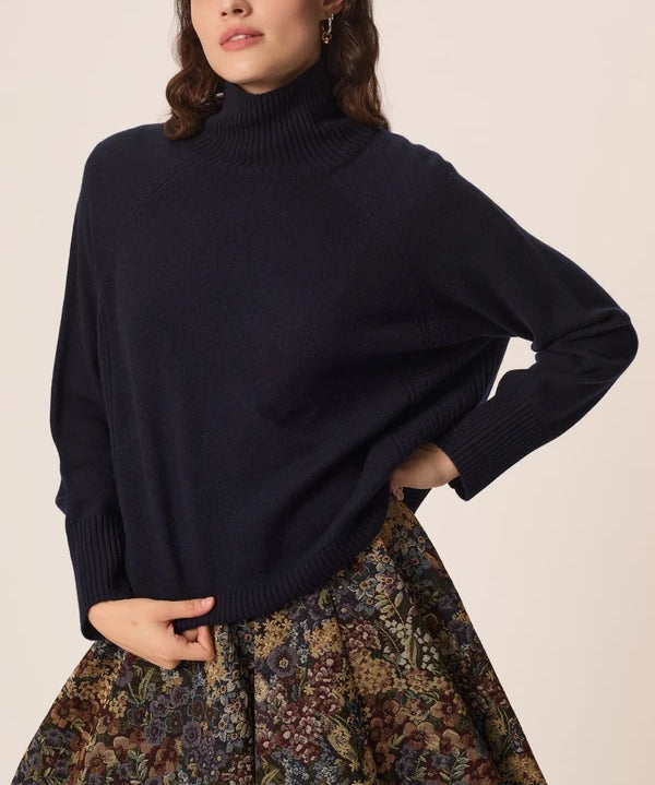 Modèle portant le pull col roulé marine Aramis DES PETITS HAUTS ajustant le bas du tricot avec une jupe fleurie