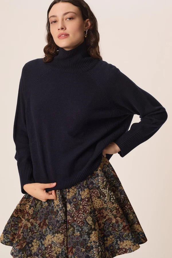 Modèle portant le pull col roulé marine Aramis DES PETITS HAUTS ajustant le bas du tricot avec une jupe fleurie