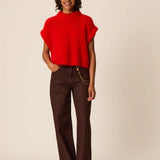 Modèle portant le pull sans manches oversize rouge Alize DES PETITS HAUTS avec un pantalon large marron et des sandales plates