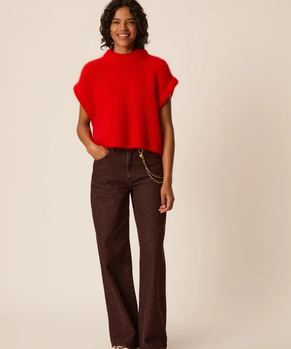 Modèle portant le pull sans manches oversize rouge Alize DES PETITS HAUTS avec un pantalon large marron et des sandales plates