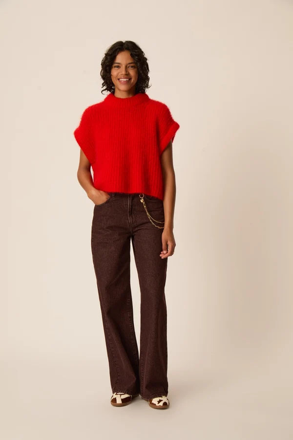 Modèle portant le pull sans manches oversize rouge Alize DES PETITS HAUTS avec un pantalon large marron et des sandales plates