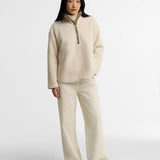 Look complet avec le pull polaire Merys beige Barbour, un jean large écru et des baskets