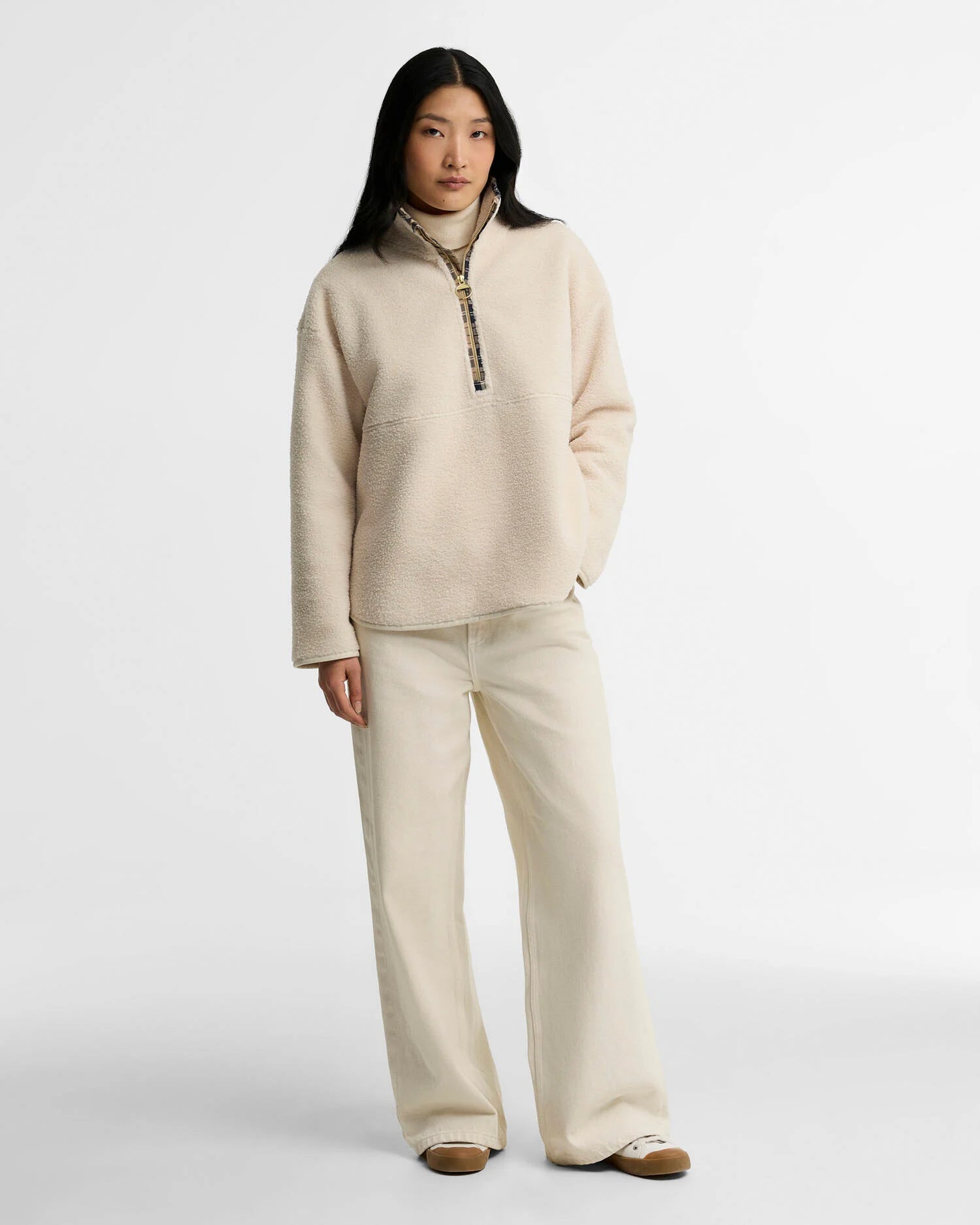 Look complet avec le pull polaire Merys beige Barbour, un jean large écru et des baskets