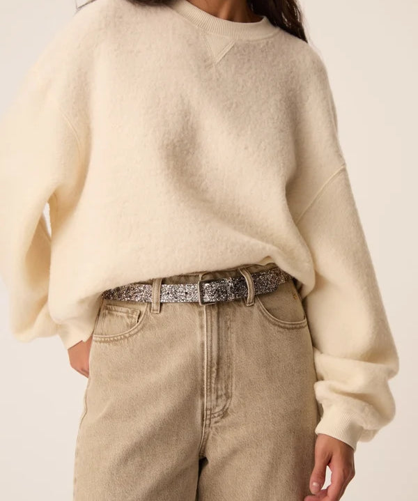 Gros plan sur le sweat écru Jonas DES PETITS HAUTS associé à un jean et une ceinture pailletéelarge
