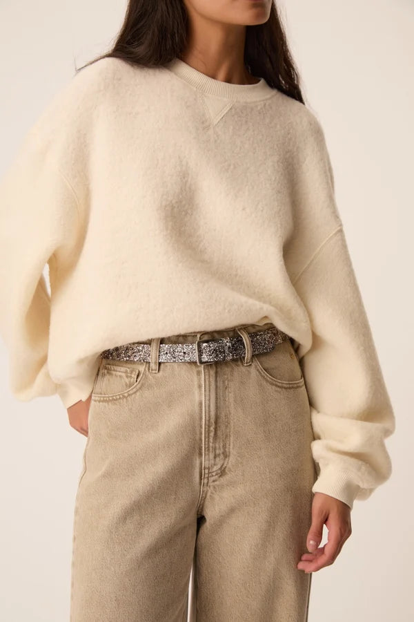 Gros plan sur le sweat écru Jonas DES PETITS HAUTS associé à un jean et une ceinture pailletéelarge
