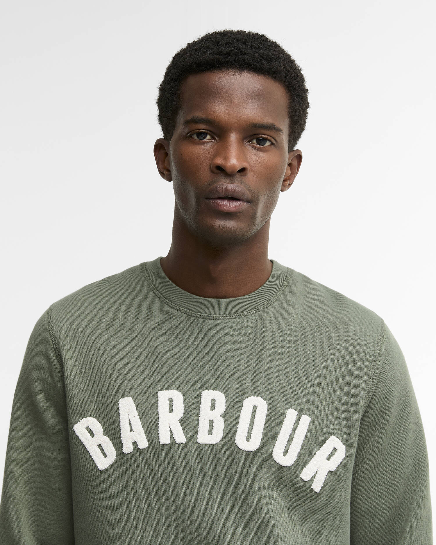 Gros plan du buste montrant le logo Barbour brodé en arc de cercle sur le sweat vert thym