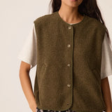 Modèle portant la veste sans manches vert forêt Zlata DES PETITS HAUTS sur un t-shirt blanc et une jupe imprimée