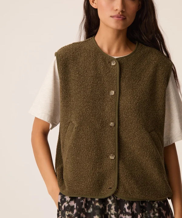 Modèle portant la veste sans manches vert forêt Zlata DES PETITS HAUTS sur un t-shirt blanc et une jupe imprimée