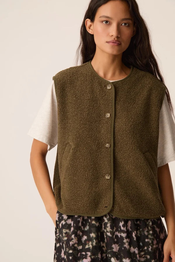 Modèle portant la veste sans manches vert forêt Zlata DES PETITS HAUTS sur un t-shirt blanc et une jupe imprimée