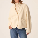 Modèle portant la veste court en maille bouclette crème Zlavina DES PETITS HAUTS avec un jean brut et un pull col roulé