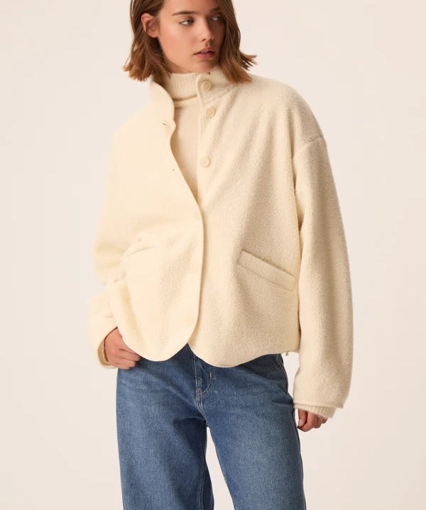 Modèle portant la veste court en maille bouclette crème Zlavina DES PETITS HAUTS avec un jean brut et un pull col roulé