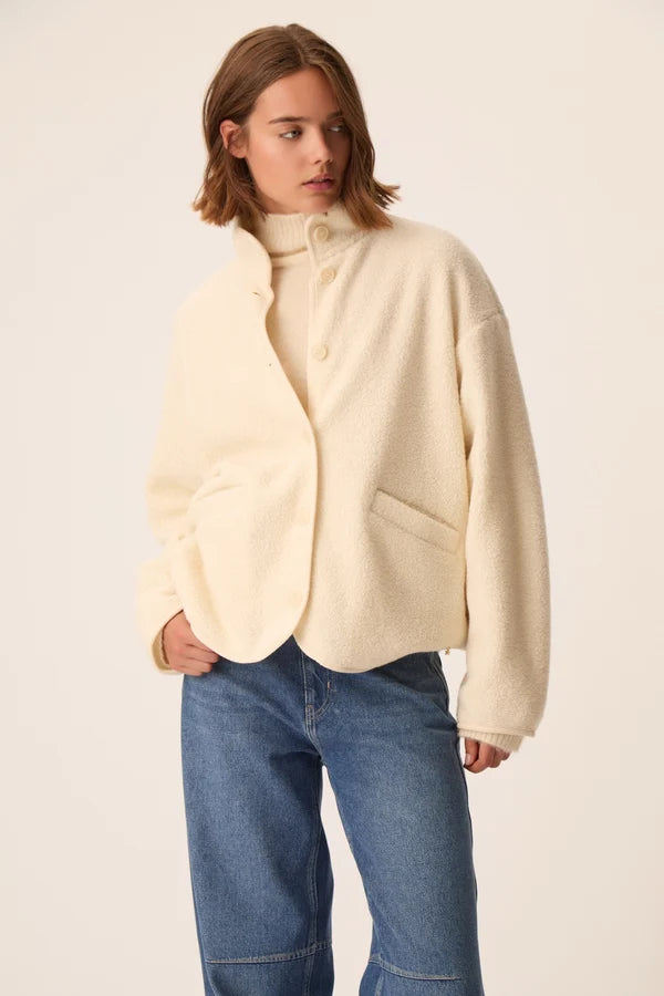 Modèle portant la veste court en maille bouclette crème Zlavina DES PETITS HAUTS avec un jean brut et un pull col roulé