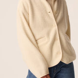 Modèle portant la veste court en maille bouclette crème Zlavina DES PETITS HAUTS avec un jean brut