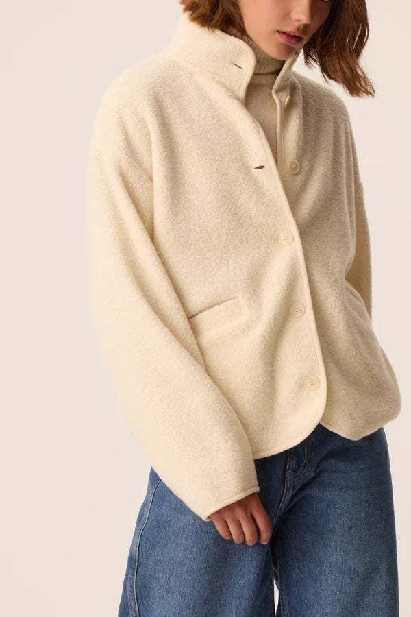 Modèle portant la veste court en maille bouclette crème Zlavina DES PETITS HAUTS avec un jean brut