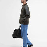 Vue de profil du mannequin portant la veste ciree courte Bedale vert fougere BARBOUR HOMME fermee avec un pantalon jean et des chaussures bateaux