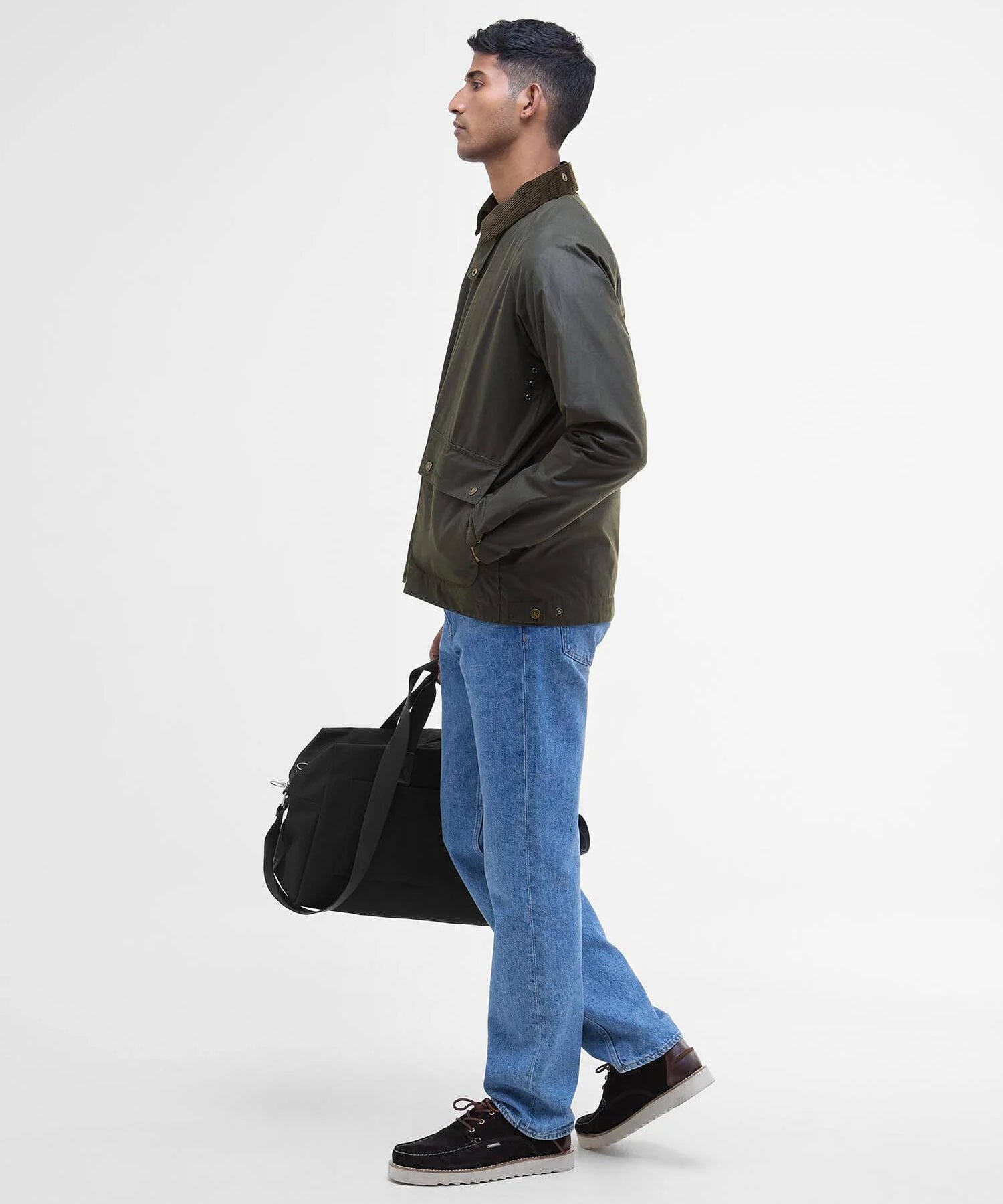 Vue de profil du mannequin portant la veste ciree courte Bedale vert fougere BARBOUR HOMME fermee avec un pantalon jean et des chaussures bateaux