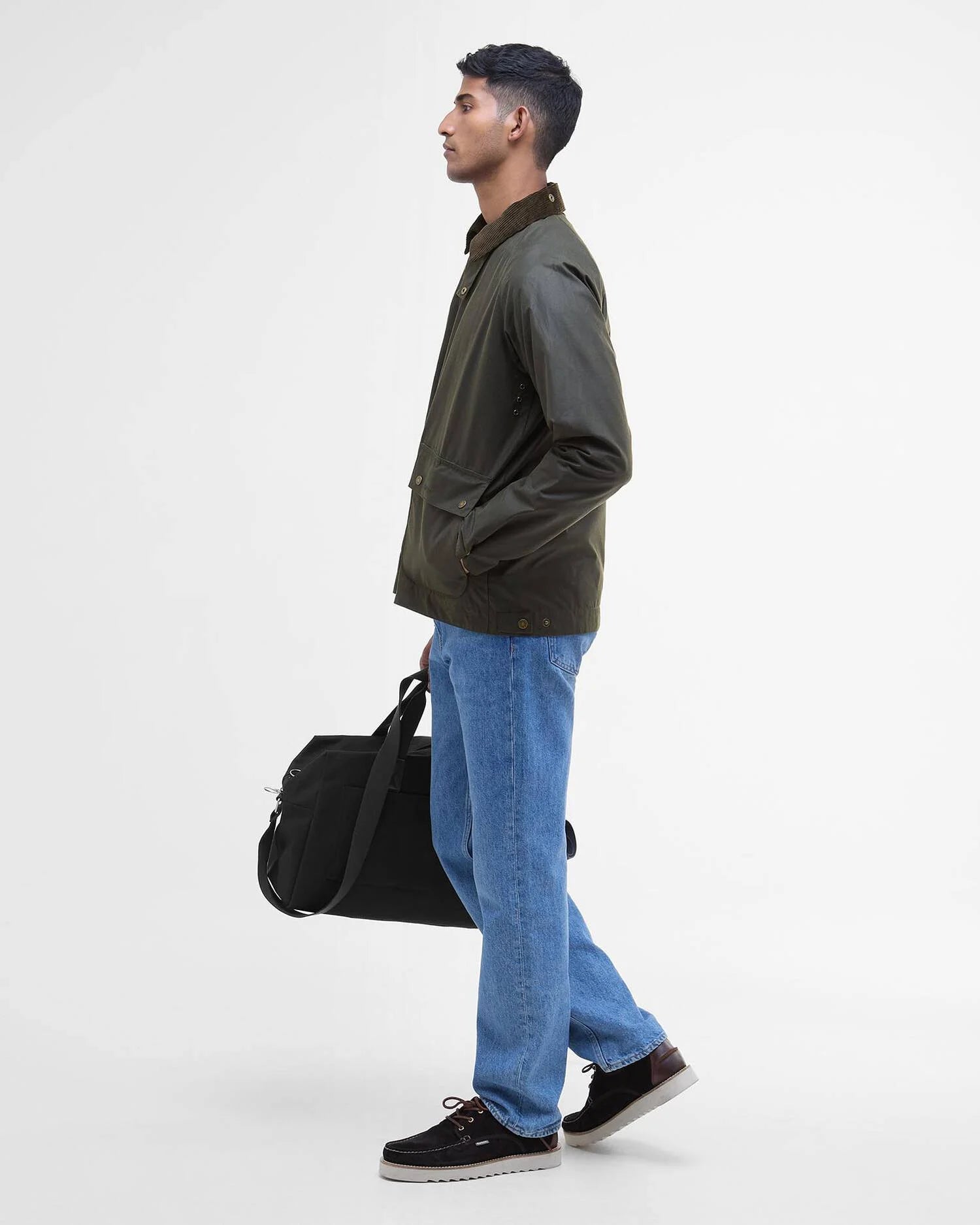 Vue de profil du mannequin portant la veste ciree courte Bedale vert fougere BARBOUR HOMME fermee avec un pantalon jean et des chaussures bateaux