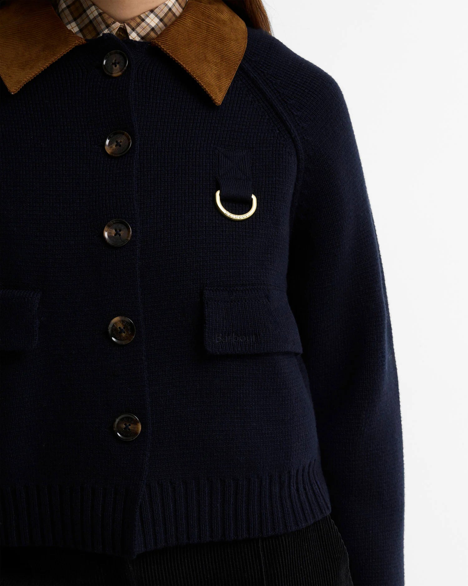 Gros plan sur la maille marine, les boutons effet corne, l'anneau en D doré et le col en velours de la veste Alverstone Barbour